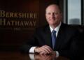 Greg Abel en sala corporativa junto al logo de Berkshire Hathaway