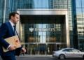 Hombre de traje azul lleva portafolios de Halliburton ante edificio de Barclays.