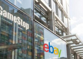 Vista de primer plano de los logotipos de GameStop y eBay en la fachada de vidrio de un edificio.
