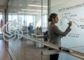 Mujer dibuja gráfico sobre los márgenes de OpenAI y Anthropic en pizarra transparente