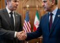 Antony Blinken y Hossein Amir-Abdollahian dándose la mano con banderas de EE.UU. e Irán detrás.
