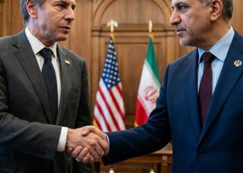 Antony Blinken y Hossein Amir-Abdollahian dándose la mano con banderas de EE.UU. e Irán detrás.
