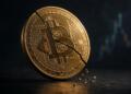 Moneda de Bitcoin con una grieta visible sobre fondo oscuro.