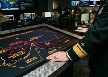 Un oficial naval de alto rango junto a una mesa táctica que muestra un mapa del Estrecho de Ormuz.