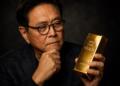 Robert Kiyosaki observa una barra de oro con expresión reflexiva.