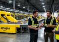 Empleados de Amazon con chalecos de seguridad hablan junto a cintas transportadoras automatizadas.