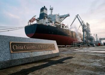Primer plano de un cartel de aduanas de granito con un gran supertanque de fondo en el puerto