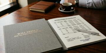 Carpeta de Wall Street abierta con informe de dividendos, bolígrafo de platino y café.