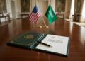 Documento oficial del pacto nuclear y banderas de EE. UU. y Arabia Saudita sobre una mesa.