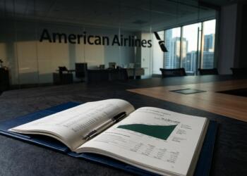 Un libro abierto con el informe de resultados de American Airlines y un bolígrafo en una mesa.