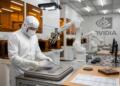 Un ingeniero de sala limpia de OpenAI sostiene una oblea de silicio sobre una bandeja de la misma empresa dentro de un laboratorio de alta tecnología con robots de NVIDIA.