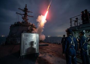 Marinos observan el lanzamiento nocturno de un misil desde un buque de guerra.