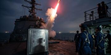 Marinos observan el lanzamiento nocturno de un misil desde un buque de guerra.