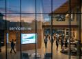 Vista exterior de oficinas de ServiceNow con empleados y una pantalla con crecimiento del 24.5%.