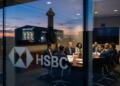 Ejecutivos de HSBC participan en una reunión en una sala de juntas con vista a las instalaciones de SpaceX al atardecer.