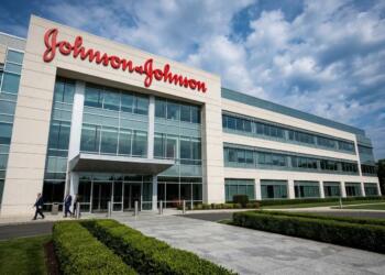 Vista exterior del edificio moderno de oficinas de Johnson & Johnson con empleados caminando cerca de la entrada.