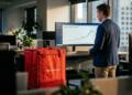 Hombre de pie frente a una pantalla con gráficos de DoorDash y una bolsa térmica roja.
