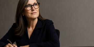 Cathie Wood junto al logo de AMD integrado en su escritorio de trabajo.