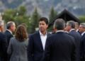 Banqueros en traje conversan en evento al aire libre con montañas de fondo.