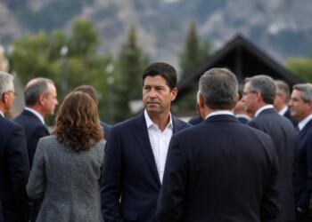 Banqueros en traje conversan en evento al aire libre con montañas de fondo.