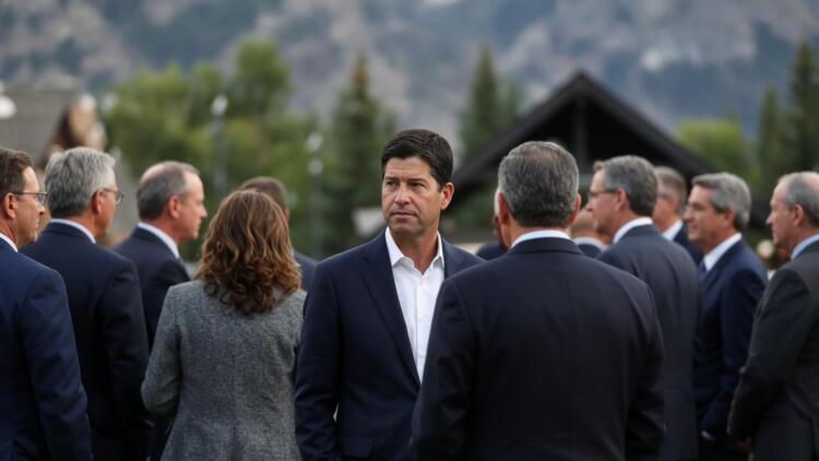 Banqueros en traje conversan en evento al aire libre con montañas de fondo.