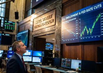 Hombre de traje observa pantallas gigantes en el piso de operaciones de Wall Street.