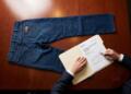 Persona revisa un informe financiero de UBS junto a unos jeans sobre una mesa de madera.