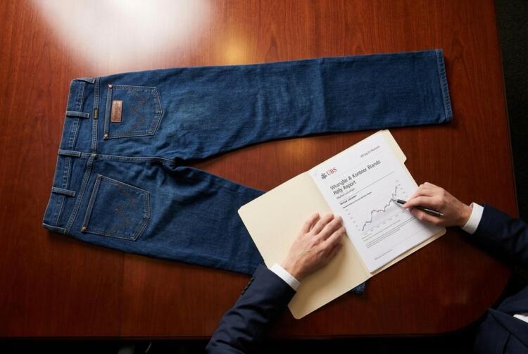 Persona revisa un informe financiero de UBS junto a unos jeans sobre una mesa de madera.