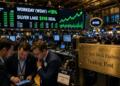 Tres hombres revisan datos frente a una pantalla del NYSE que anuncia un acuerdo de 51B.