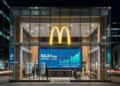 Fachada de cristal de un local de McDonald's con pantalla interior que muestra gráficos.