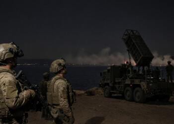 Soldados equipados vigilan un vehículo militar con lanzador de misiles junto a la costa.