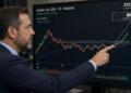 Operador financiero apunta a una pantalla con gráficos bursátiles de la empresa Zscaler.