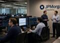Operadores y analistas de JPMorgan revisan pantallas con cotizaciones de crudo y datos.