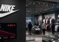 Pantalla frente a tienda Nike muestra gráficos bursátiles con caída del valor y precio.