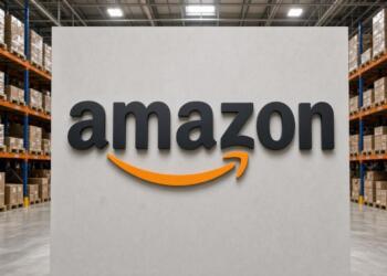 Logo de Amazon sobre muro en centro de distribución con estanterías.
