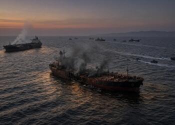 Barcos cargueros humeantes y dañados navegando en el mar durante un atardecer nublado.