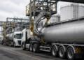 Fila de camiones cisterna estacionados en una planta industrial con brazos de carga.