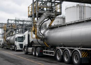 Fila de camiones cisterna estacionados en una planta industrial con brazos de carga.
