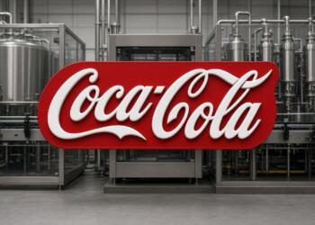 Logo de Coca-Cola frente a maquinaria de planta embotelladora.