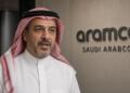 Un directivo de Saudi Aramco con vestimenta tradicional frente al logotipo de la empresa.