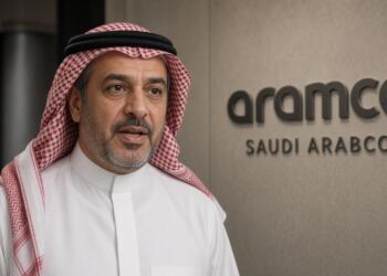 Un directivo de Saudi Aramco con vestimenta tradicional frente al logotipo de la empresa.