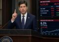 Un orador de la Reserva Federal gesticula frente a pantallas con datos del S&P 500 y el IPP.