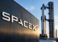 Logotipo de SpaceX en un hangar frente a un cohete en su plataforma.