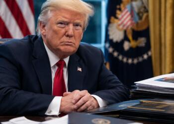 Donald Trump sentado ante documentos y carpetas en su escritorio.